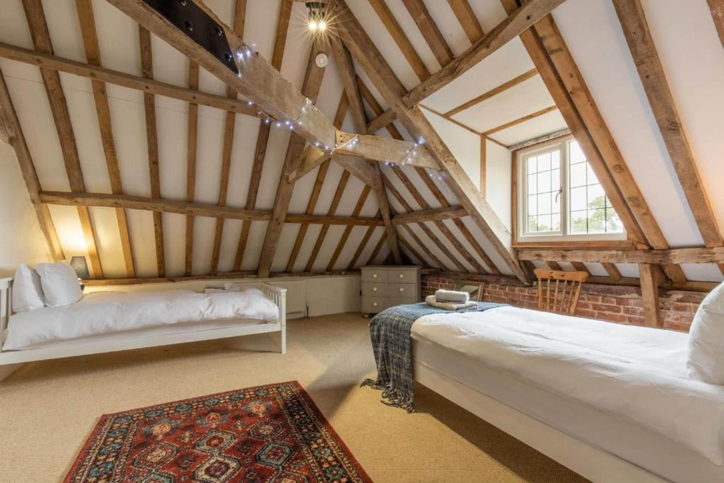 A loft bedroom with a sloped ceiling, two beds, a small dresser, and a window.