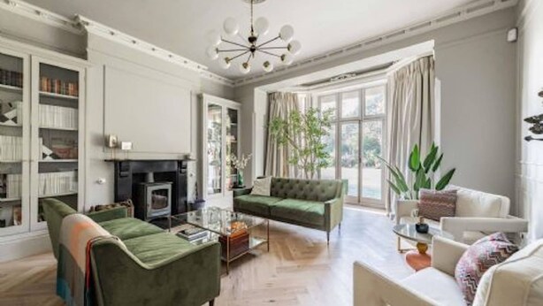 A spacious living room with a fireplace, green and white sofas, a coffee table, and a large window with curtains. - Host Stay Bressingham Lodge (Diss)