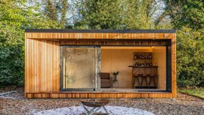 A modern, compact cabin with a sliding glass door entrance, a small outdoor seating area, and a visible kitchen area with bar stools. - Host Stay Bressingham Lodge (Diss)