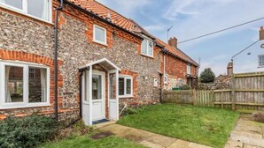 A two-story stone house with a white door and windows, a small front yard, and a wooden fence. - Host Stay 2 Ruscon Cottage (King's Lynn)