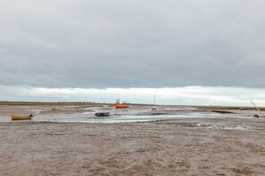 A muddy, open landscape with a few boats and a distant orange structure. - Host Stay 2 Ruscon Cottage (King's Lynn)