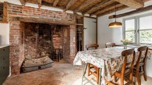 Una habitación rústica con vigas de madera a la vista, chimenea de ladrillo, una mesa de comedor con sillas y una ventana con vistas a zonas verdes.