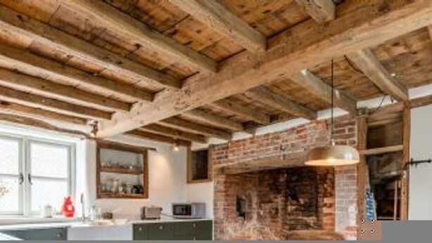 Una cocina con vigas de madera a la vista, chimenea de ladrillo y muebles de cocina modernos.