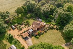 An aerial view of a large, rustic house surrounded by lush greenery and a well-maintained lawn.