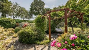 A garden with a wooden pergola, a hanging chair, and blooming flowers.