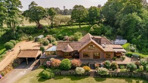 A large, two-story house with a stone facade, surrounded by lush gardens and a well-maintained lawn.