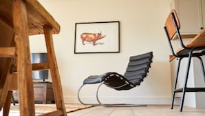 A wooden dining table with chairs, a black lounge chair, and a framed animal picture on the wall. - Host Stay Number Two Piglets (King's Lynn)