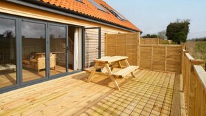 A modern house with a wooden deck, large sliding glass doors, and a tiled roof. - Host Stay Number Two Piglets (King's Lynn)