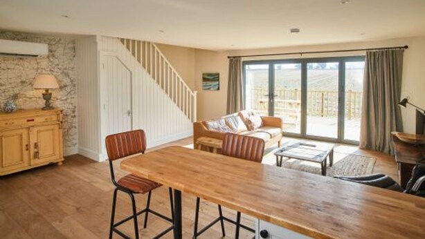 A spacious room with a wooden dining table, a sofa, and a staircase leading to an upper level. - Host Stay Number Two Piglets (King's Lynn)