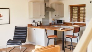 A compact kitchen with white cabinets, a wooden countertop, and a built-in microwave. There are two chairs and a table. - Host Stay Number Two Piglets (King's Lynn)