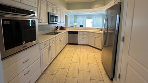 A modern kitchen with white cabinets, stainless steel appliances, and a tiled floor.