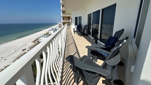 A balcony with a view of the beach, outdoor seating, and a railing.