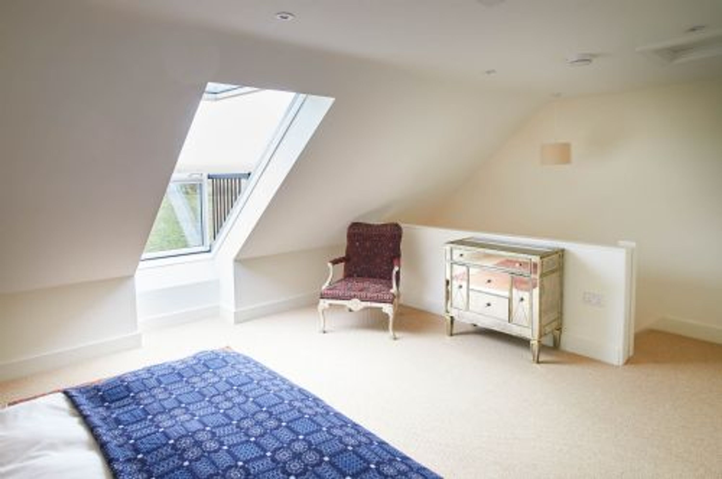 Un dormitorio con techo inclinado, una ventana, una silla y un aparador.