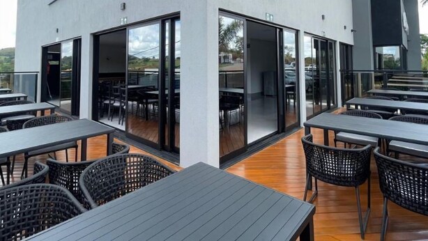 An outdoor dining area with tables and chairs, large sliding glass doors, and a modern building facade. - Escarpas Styles Hotel (Capitólio)