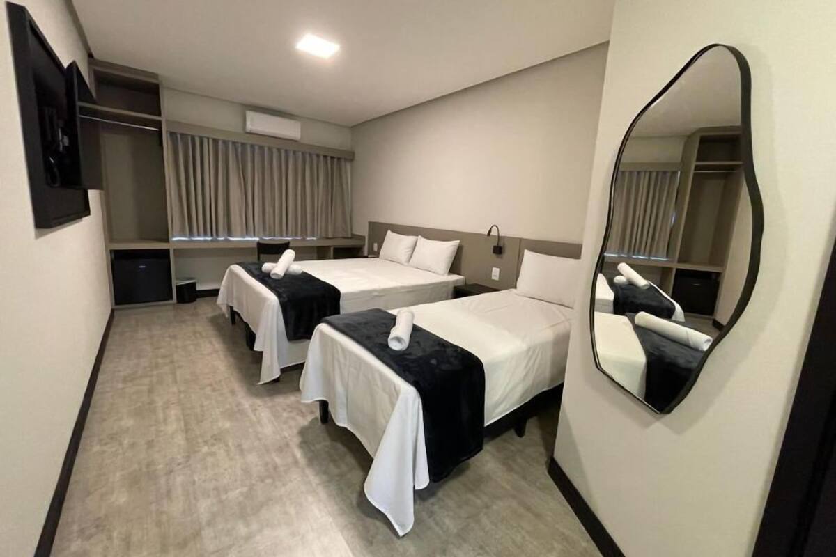 Ein Hotelzimmer mit zwei Betten, einem großen Spiegel, einem Kleiderschrank und einem Flachbildfernseher.