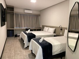 Quarto de hotel com duas camas, um guarda-roupa, um espelho e ar condicionado.