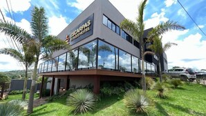 A modern hotel with a glass facade, palm trees, and a clear sky. - Escarpas Styles Hotel (Capitólio)