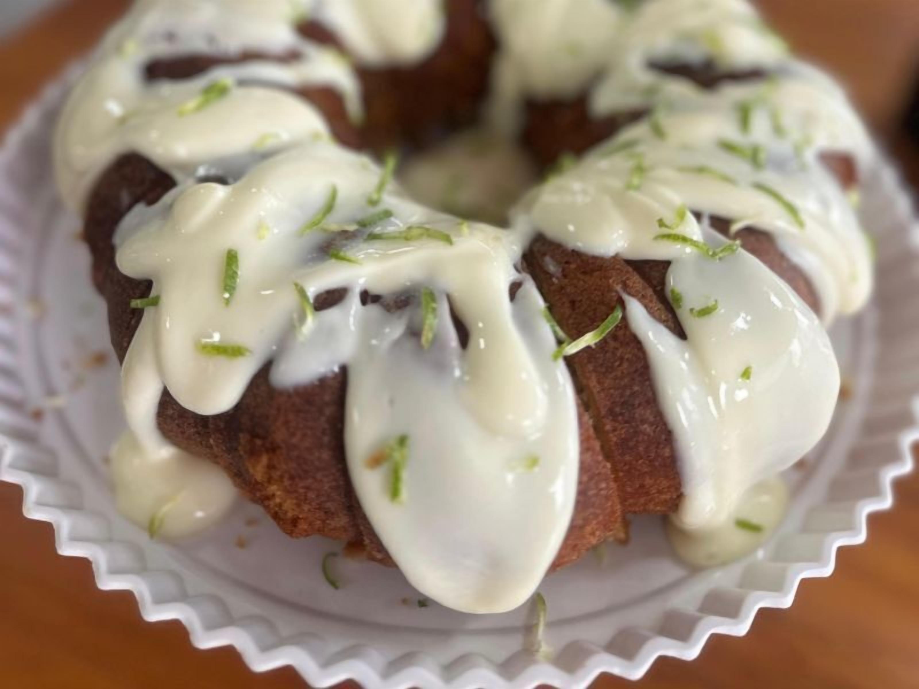 A bundt cake with white icing and green garnish on a white plate.