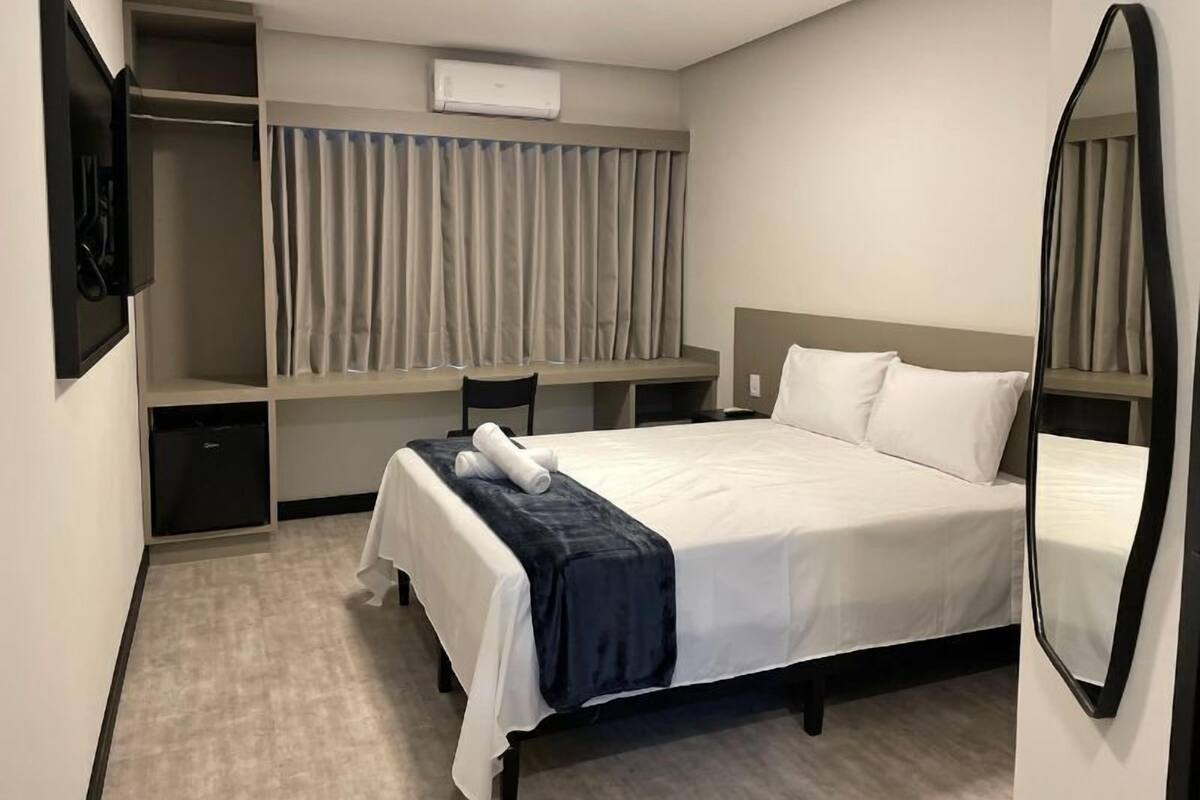 Ein Hotelzimmer mit Bett, Schreibtisch, Stuhl, Kleiderschrank und Spiegel.