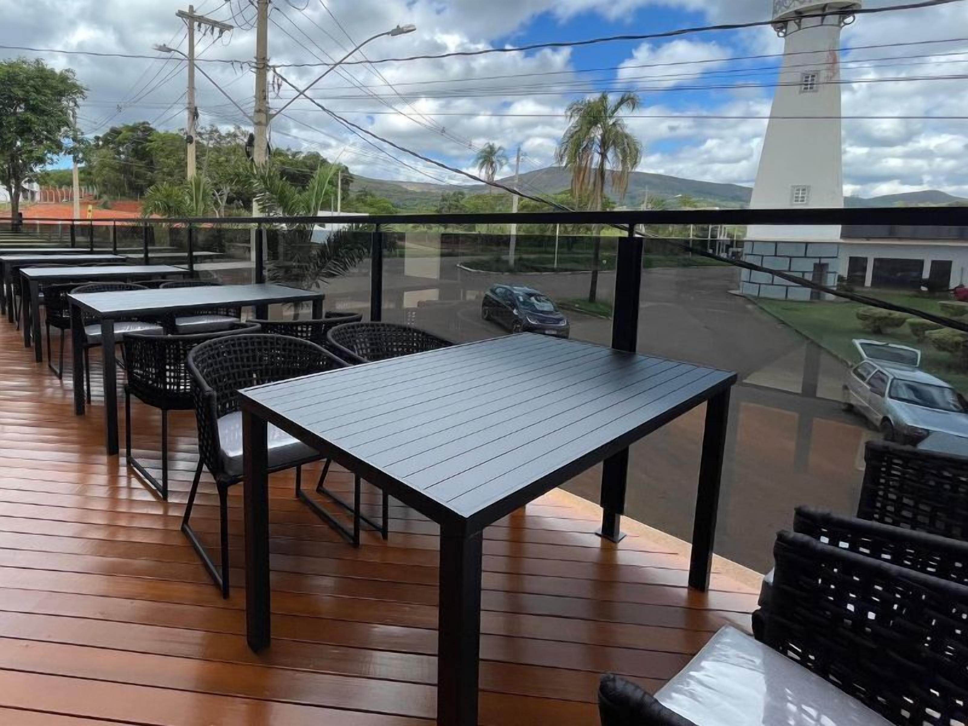 Un área de comedor al aire libre con mesas y sillas, con vistas a una calle con coches y un edificio blanco.