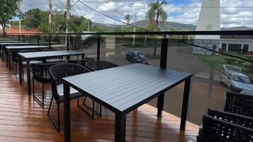 Un área de comedor al aire libre con mesas y sillas, con vistas a una calle con coches y un edificio blanco.