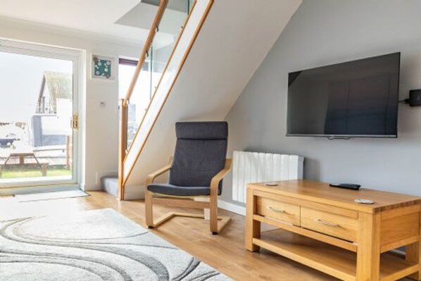A modern living room with a wooden desk, a dark chair, and a TV mounted on the wall. - Host Stay Kingsmere (Norwich)
