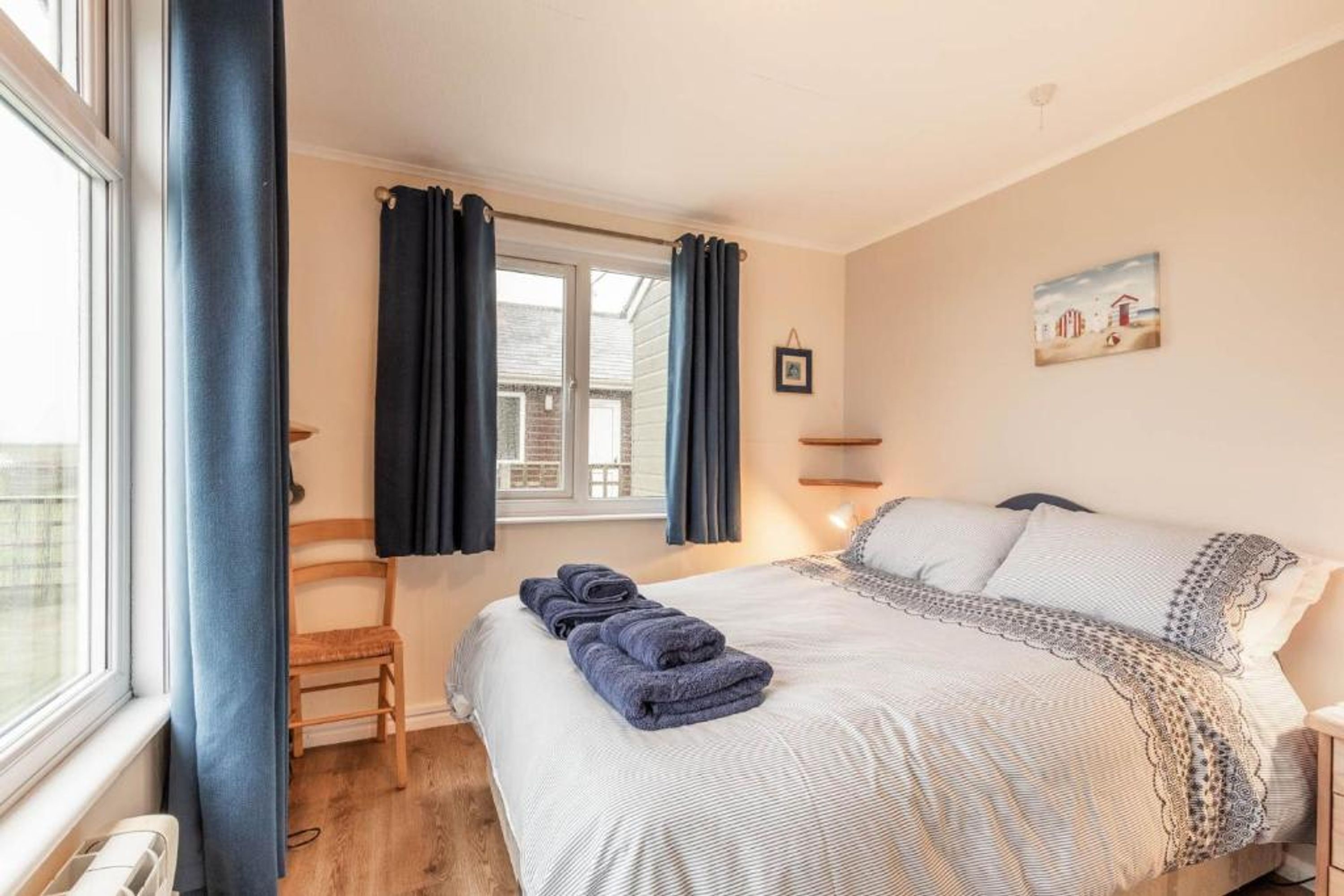 A bedroom with a bed, a chair, a window with curtains, and a painting on the wall.