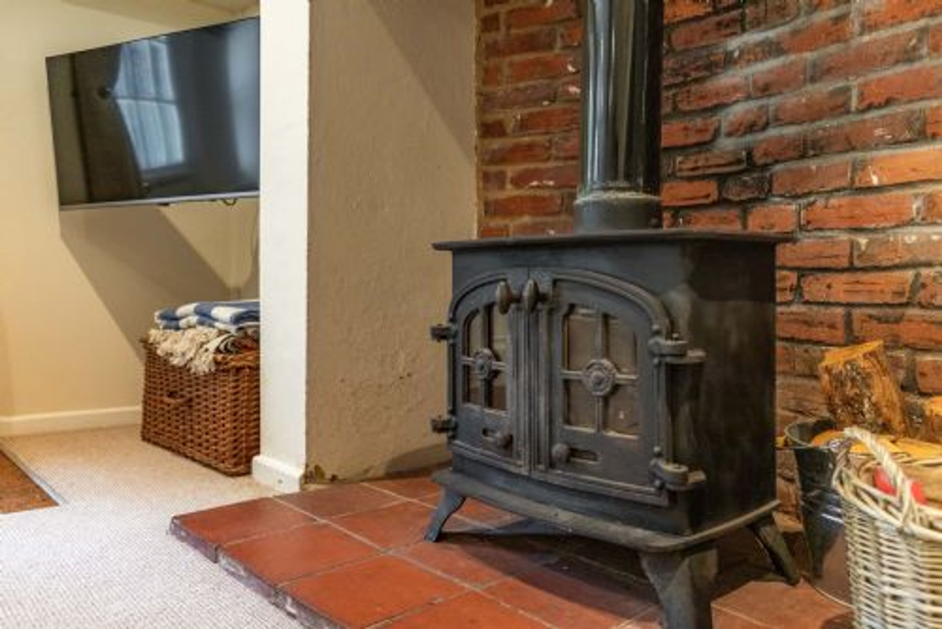 Una habitación con chimenea tradicional, televisor montado en la pared y una cesta de mimbre en el suelo.