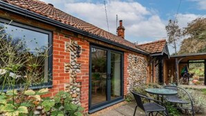 A brick house with a stone wall, a glass door, and a patio with chairs. - Host Stay The Old Church Hall (Holt)
