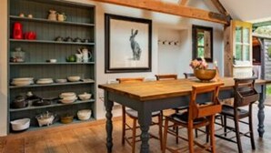 A dining area with a wooden table and chairs, a hanging light fixture, and a shelf with dishes. - Host Stay The Old Church Hall (Holt)