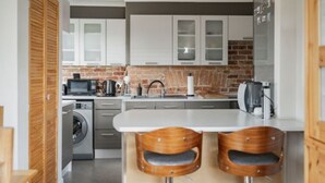 A modern kitchen with white cabinets, a brick backsplash, and a central island with two wooden bar stools. - Host Stay Manor View (Fakenham)