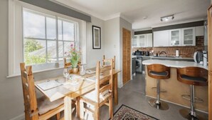 A modern kitchen with white cabinets, a central island, and a dining area with wooden chairs and a table. - Host Stay Manor View (Fakenham)