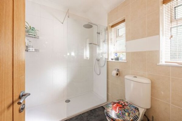 A bathroom with a glass shower enclosure, a toilet with a colorful seat cover, and a small window with blinds.