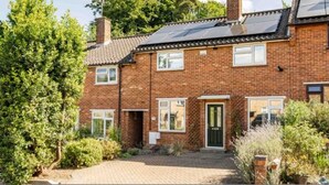 A two-story brick house with a paved driveway, a green door, and a small garden with various plants. - Host Stay Maple House (Norwich)