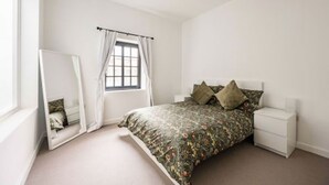 Ein Schlafzimmer mit Bett, Nachttisch, Spiegel und einem Fenster mit Vorhängen.