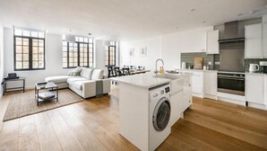 Eine moderne Küche mit Kochinsel, integriertem Waschmaschine und Essbereich mit Sofa und Tisch.