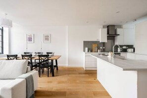 A modern kitchen with white cabinetry, a wooden dining table, and a built-in island with a sink. - Host Stay The Old Post Office (Norwich)