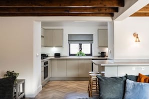 A modern kitchen with white cabinets, a herringbone wood floor, and a wooden ceiling. - Host Stay Fender Cottage (Cromer)