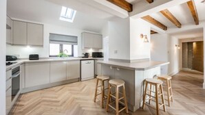 Une cuisine moderne avec des meubles blancs, un parquet à motifs en chevrons et des poutres en bois au plafond.