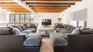 Un salon moderne doté d’un grand canapé d’angle, d’un téléviseur à écran plat et de poutres en bois au plafond.