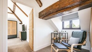 Une pièce avec un plafond en pente, une poutre en bois, une fenêtre, une chaise, une petite table et un meuble.