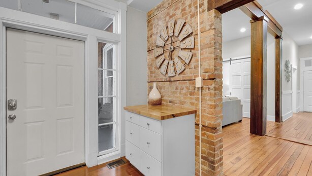 Una habitación con una puerta blanca, una pared de ladrillo con un reloj, un armario de madera y un sofá blanco.