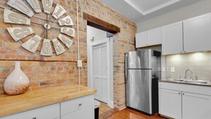 Una cocina con pared de ladrillo, armarios blancos, un refrigerador de acero inoxidable y encimera de madera.