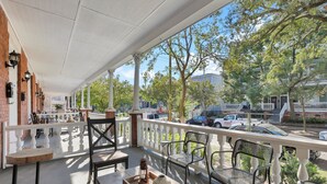 Un espacio al aire libre cubierto con columnas blancas, barandilla y varias sillas y mesas.