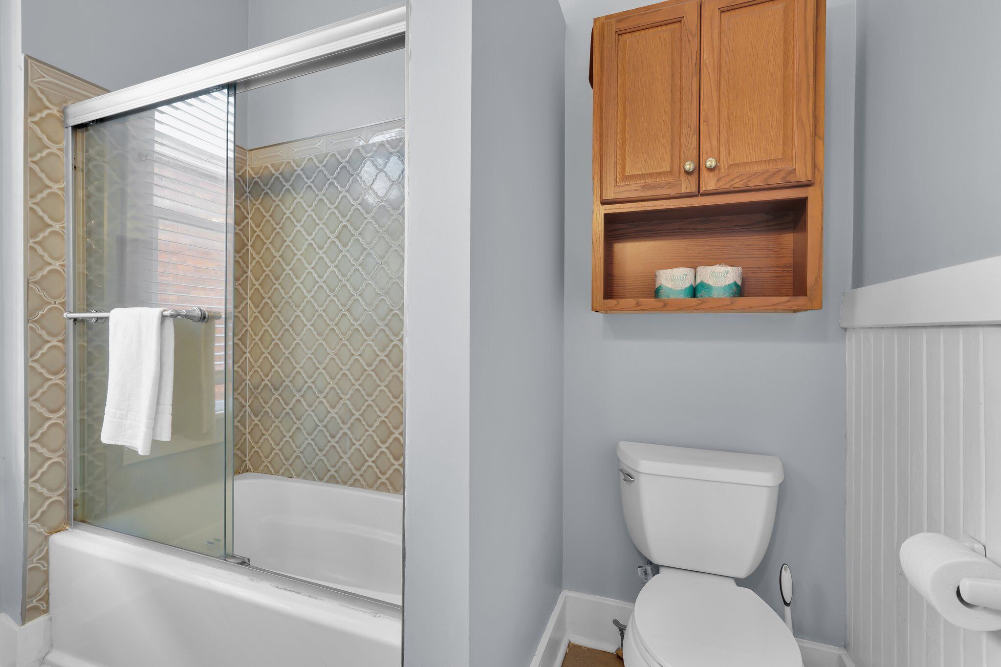 Une salle de bain avec une douche à parois de verre, des toilettes et un meuble en bois placé au-dessus des toilettes.