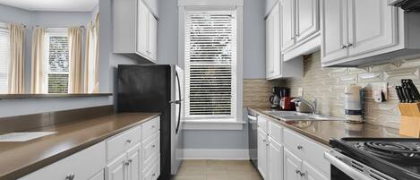 A modern kitchen with white cabinets, a black refrigerator, a window with blinds, and a tiled backsplash.