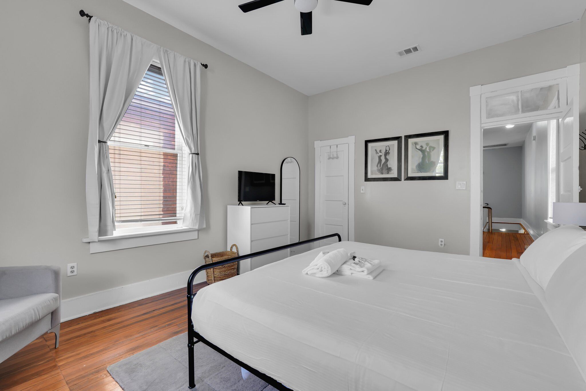 Un dormitorio con una cama, televisión, cómoda y ventana con cortinas.