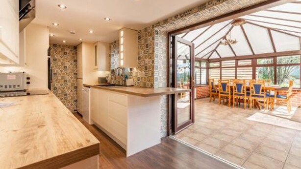 A modern kitchen with a wooden countertop, a built-in oven, and a dining area with wooden chairs and a glass door leading to an outdoor patio. - Host Stay Honeysuckle Cottage (Cromer)