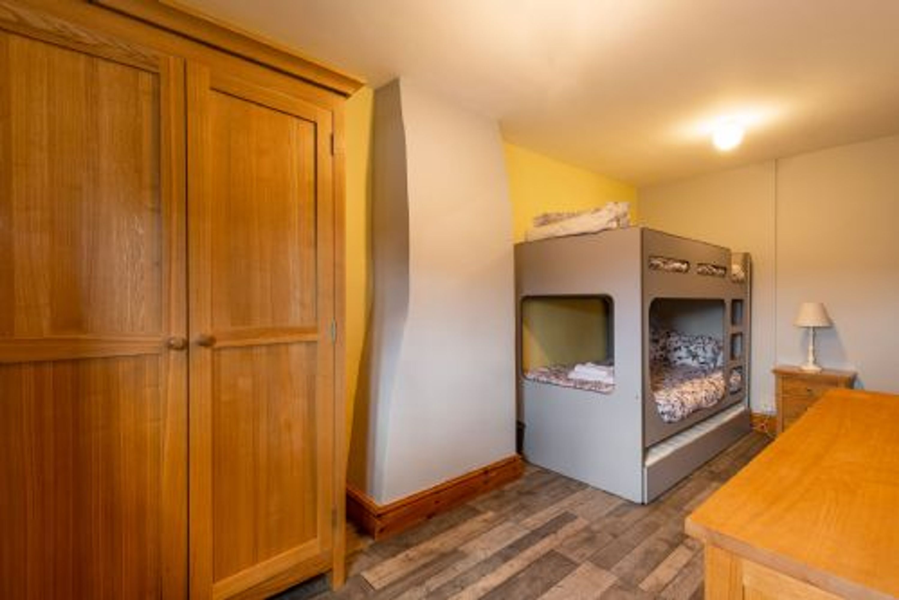 Ein Zimmer mit Etagenbett, Holzschrank und einem kleinen Tisch mit Lampe.