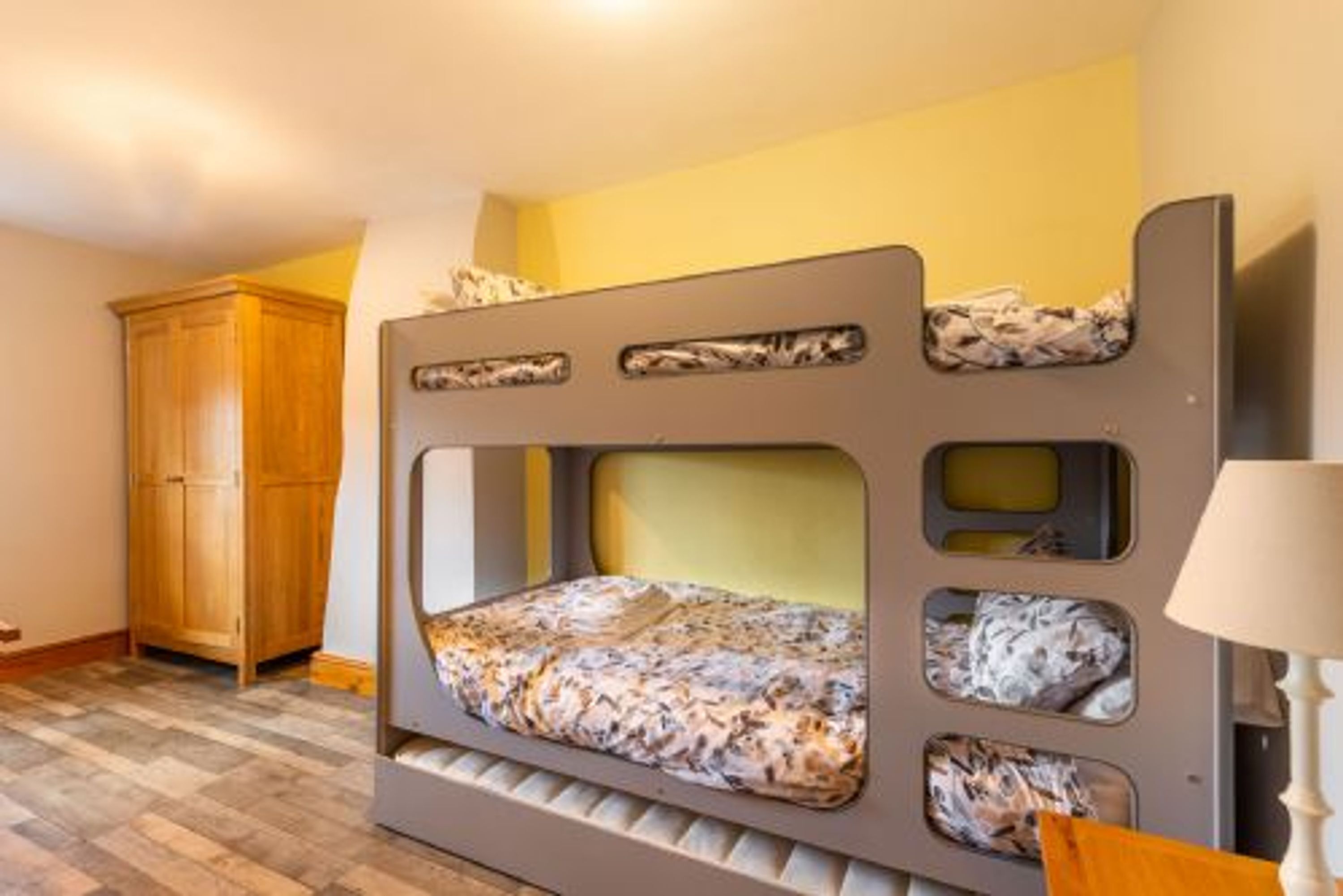 Un lit superposé avec un matelas à motifs, une armoire en bois et une lampe.